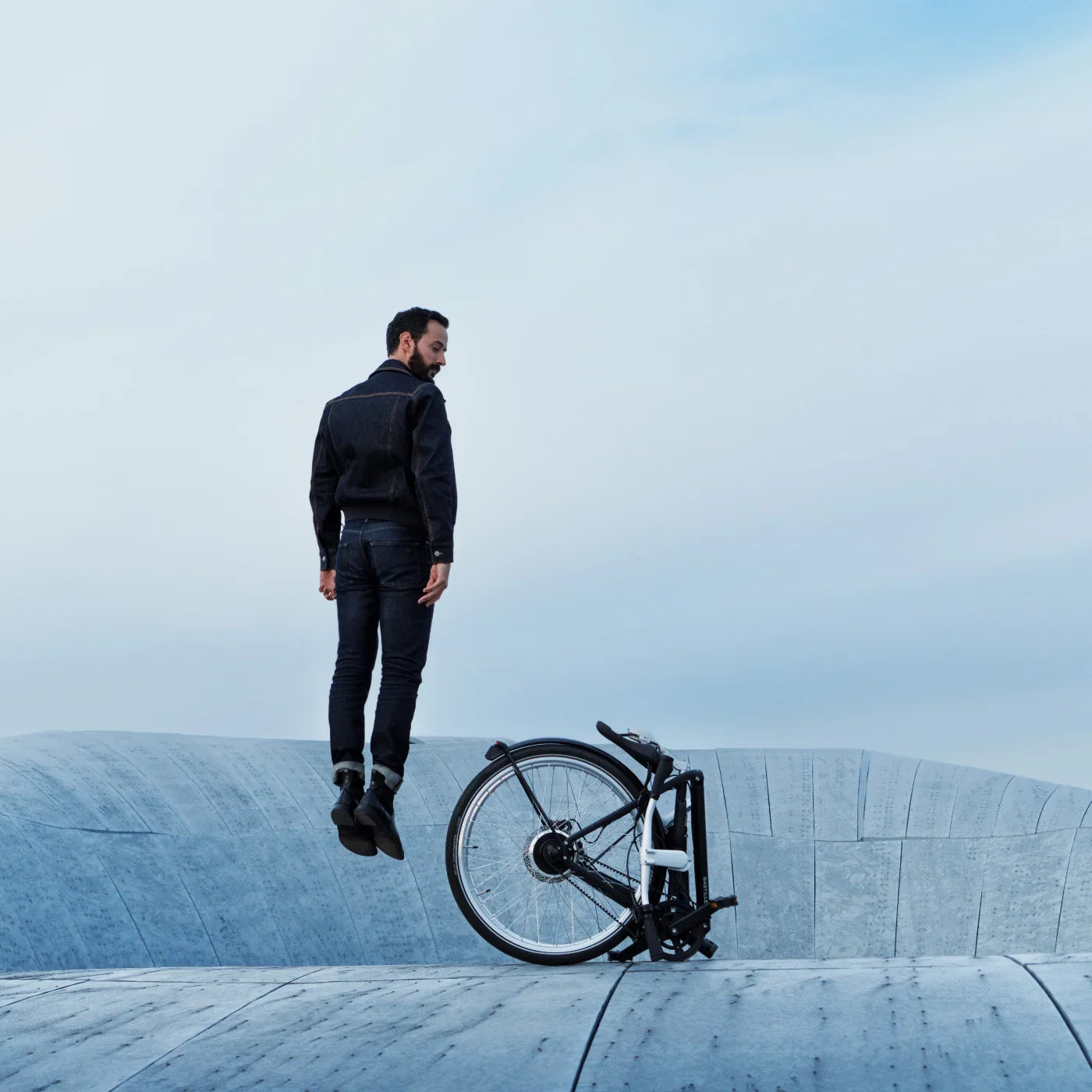 A man dressed in black jumps next to a folded up bicycle