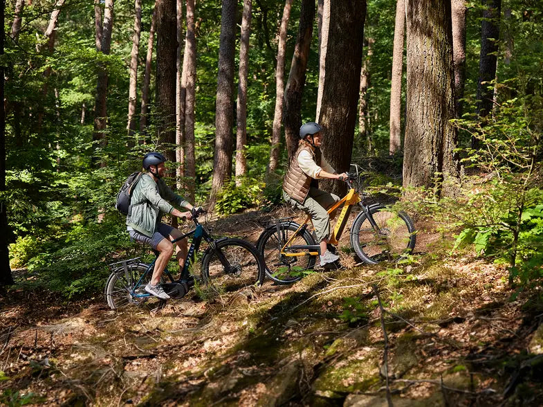 Two people riding e-bikes in the forest.
