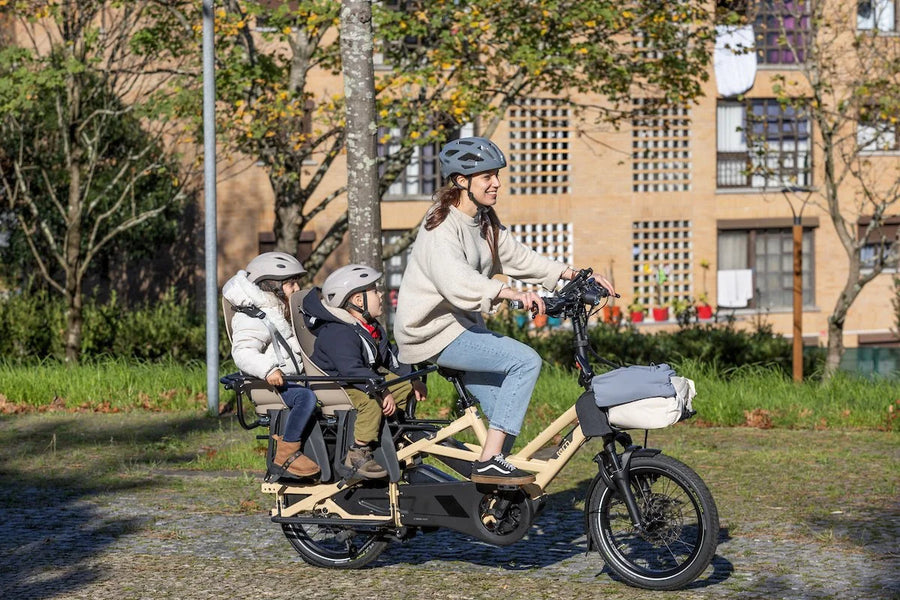 Person riding a electric bike with two children in a park-like setting.