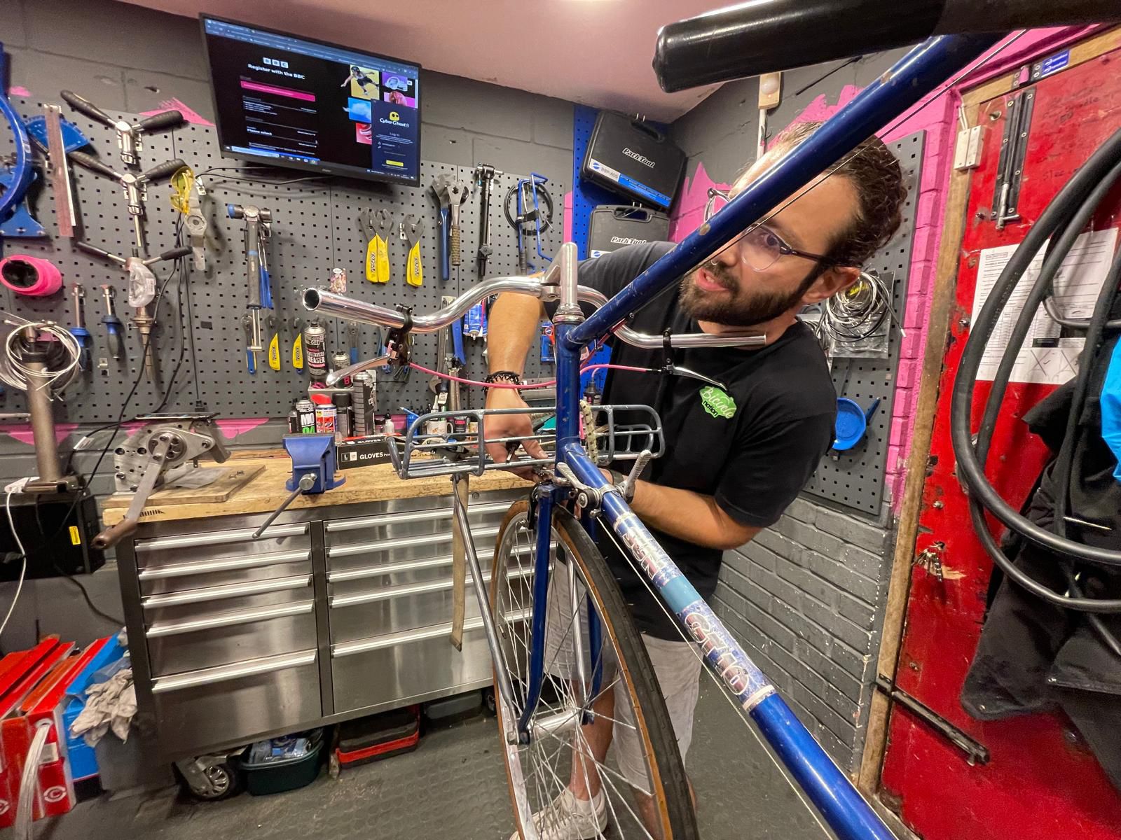 Man working on a bicycle in a workshop with tools and equipment around.