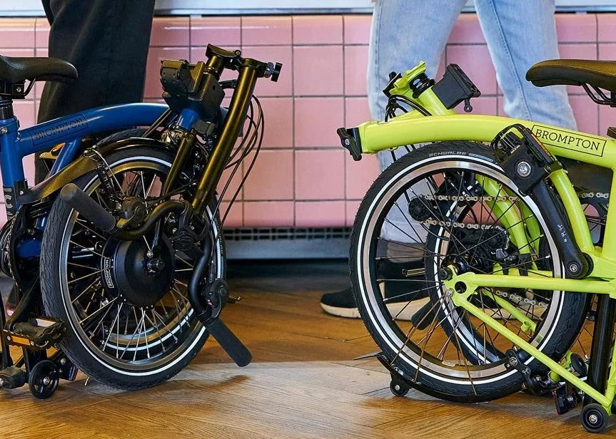 Brompton bikes, one lime colour another blue folded standing on the wooden floor.