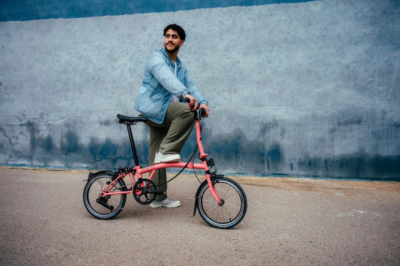 Person sitting on a pink bicycle against a textured wall.