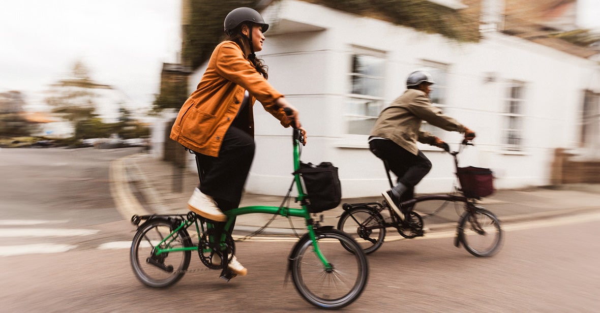Two people riding Brompton folding bikes along a city street.