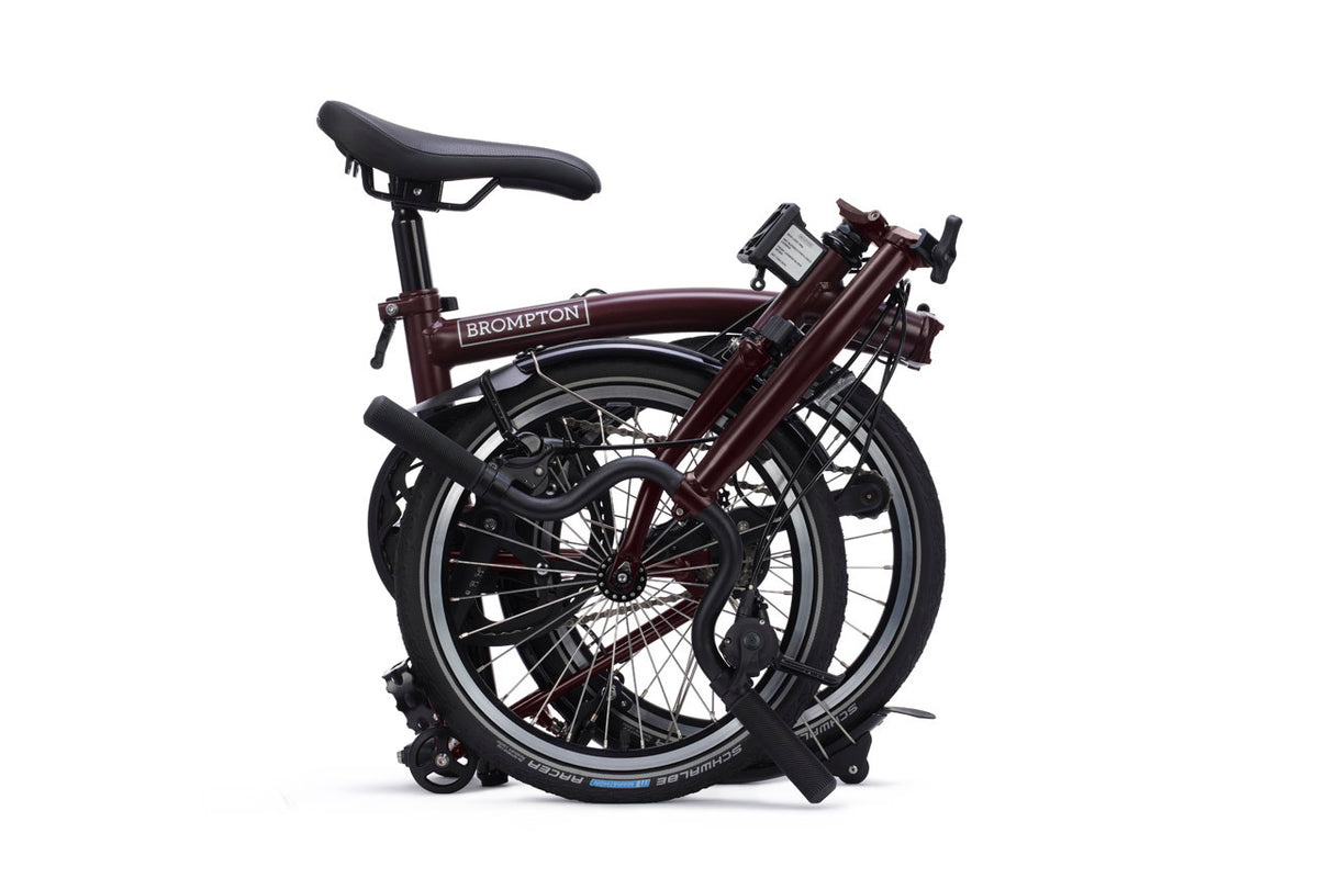 A folded Brompton folding bicycle in a dark burgundy frame with black components, shown on a clean white background.