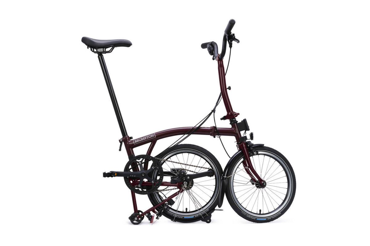 A folding bicycle with a dark burgundy frame and black components, shown folded with the rear rack extended against a plain white background.
