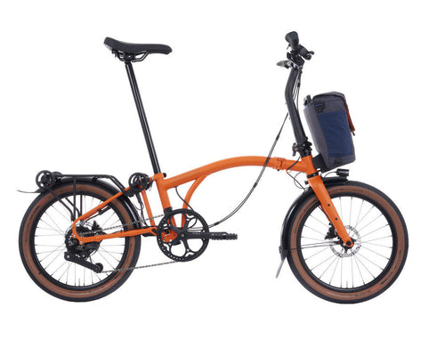Orange Brompton G Line folding bicycle with a black seat and rear storage basket on a white background