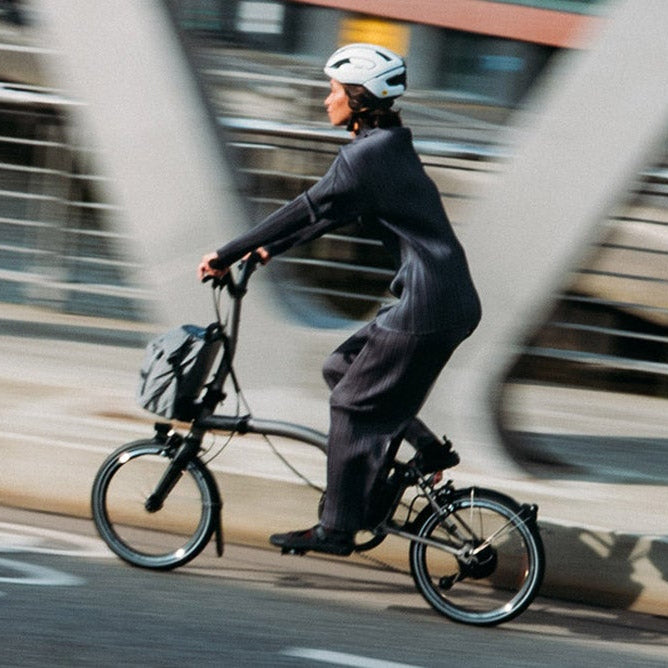 Person riding a Brompton T Line bicycle on a city street with blurred background