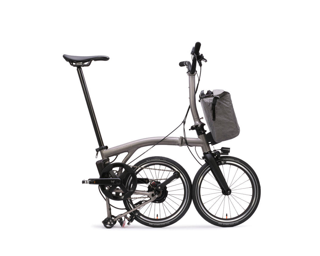 Foldable Brompton Electric T Line bicycle with a front bag on a white background