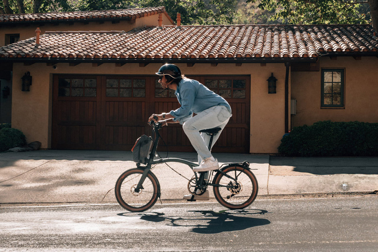 A person riding on the Brompton g Line folding bike on the road in from of the house.