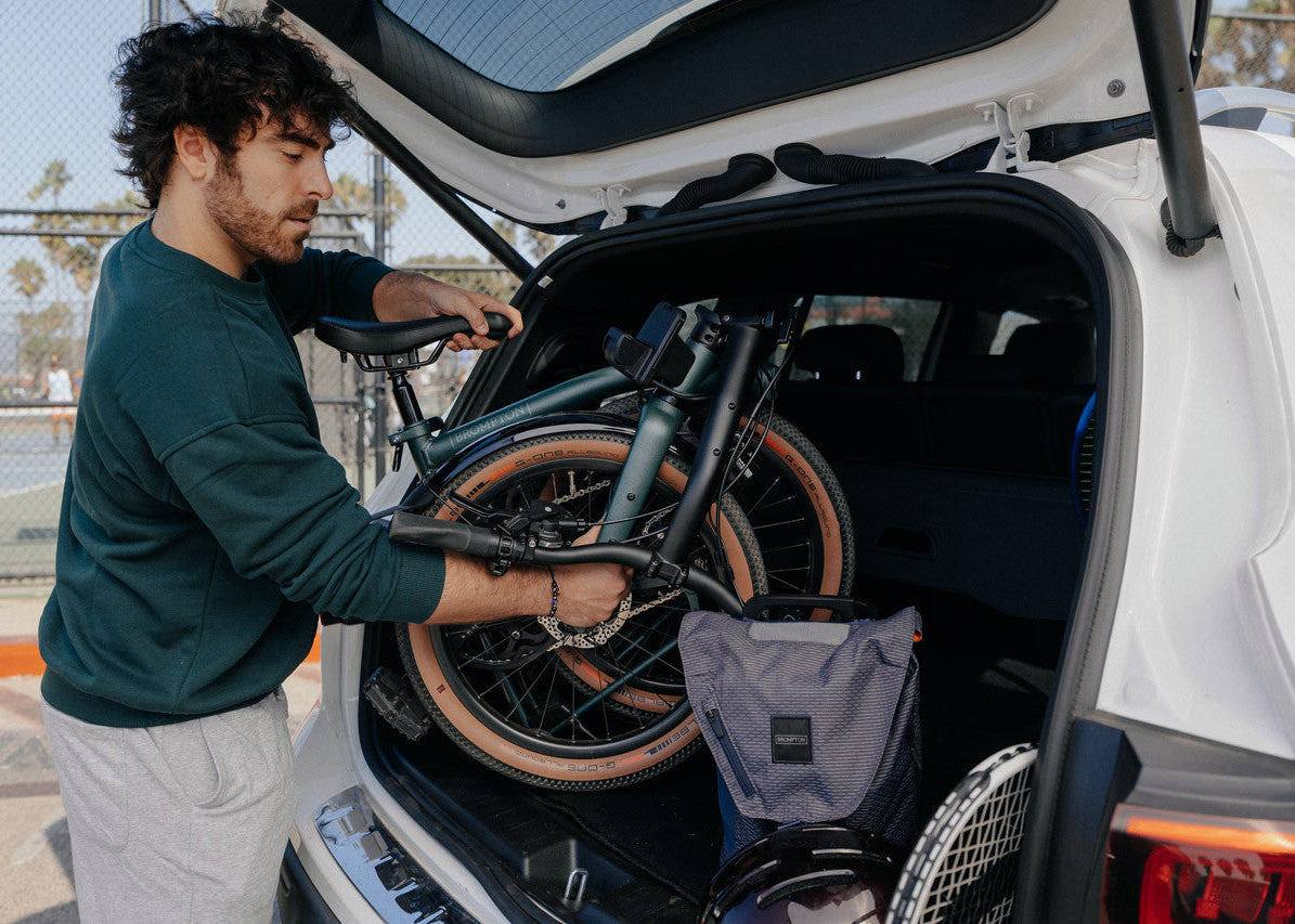 A person loading the Brompton G Line folding bike to the white car.