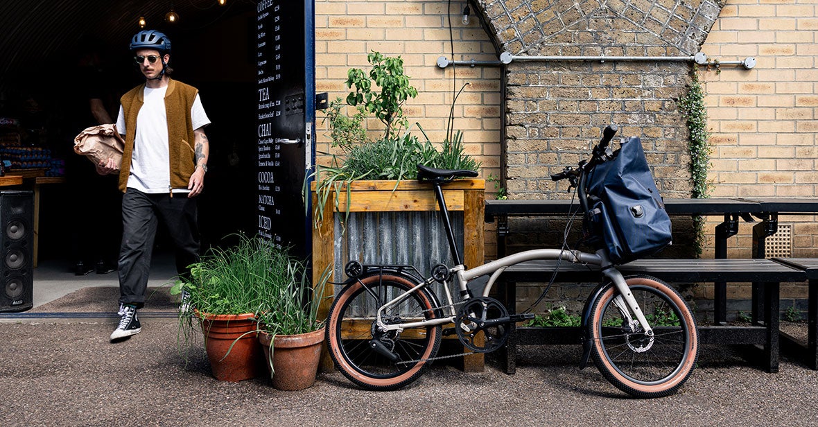 A person walking with a package next to a Brompton folding bike in an urban setting