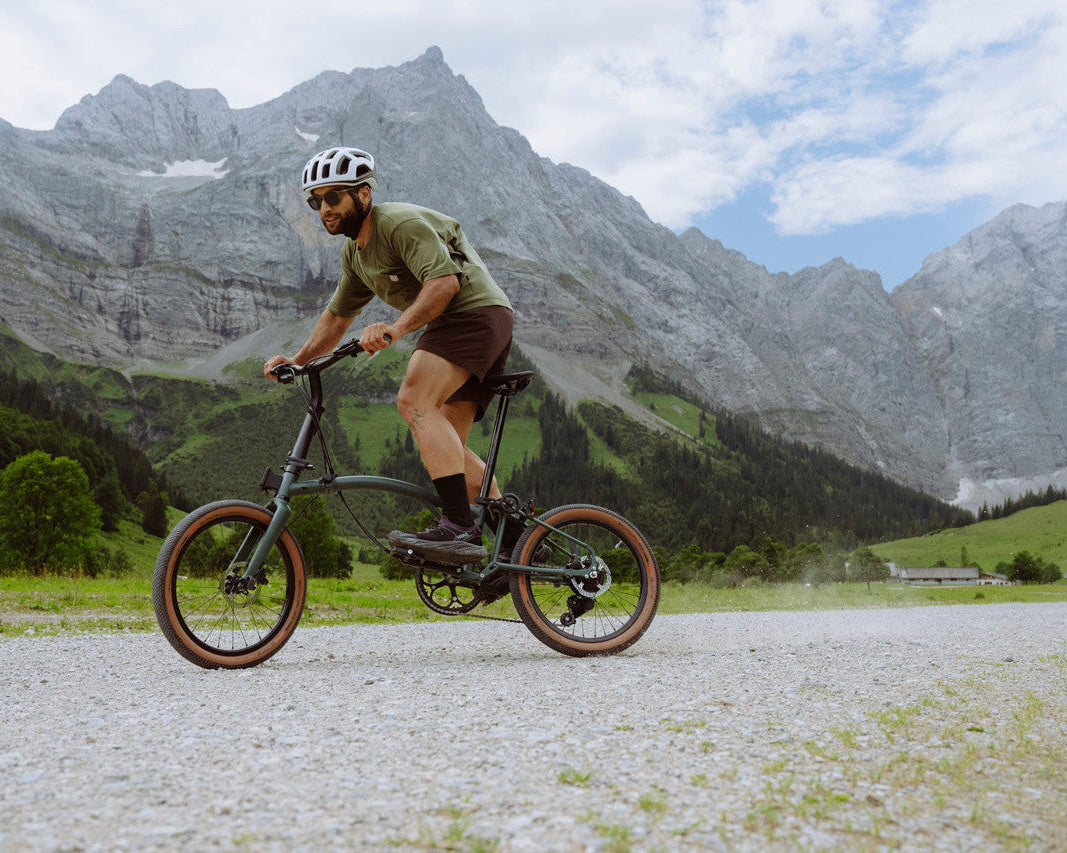 Man riding a Brompton g Line bicycle on a gravel path with mountains in the background