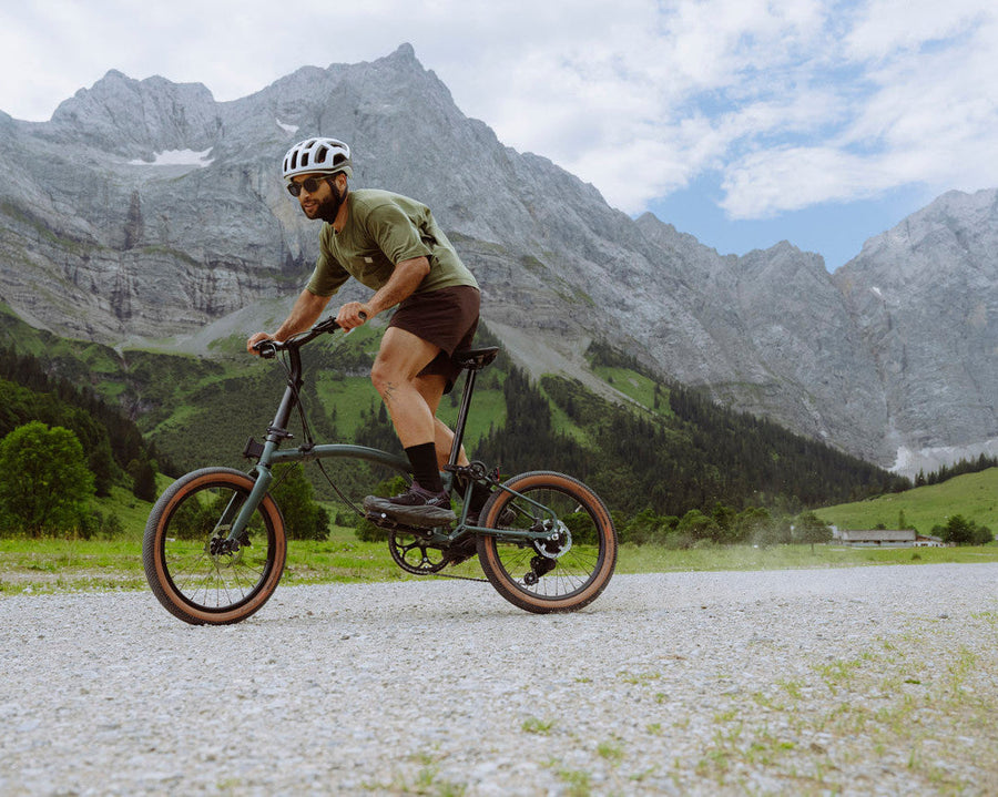 Man riding a Brompton g Line bicycle on a gravel path with mountains in the background
