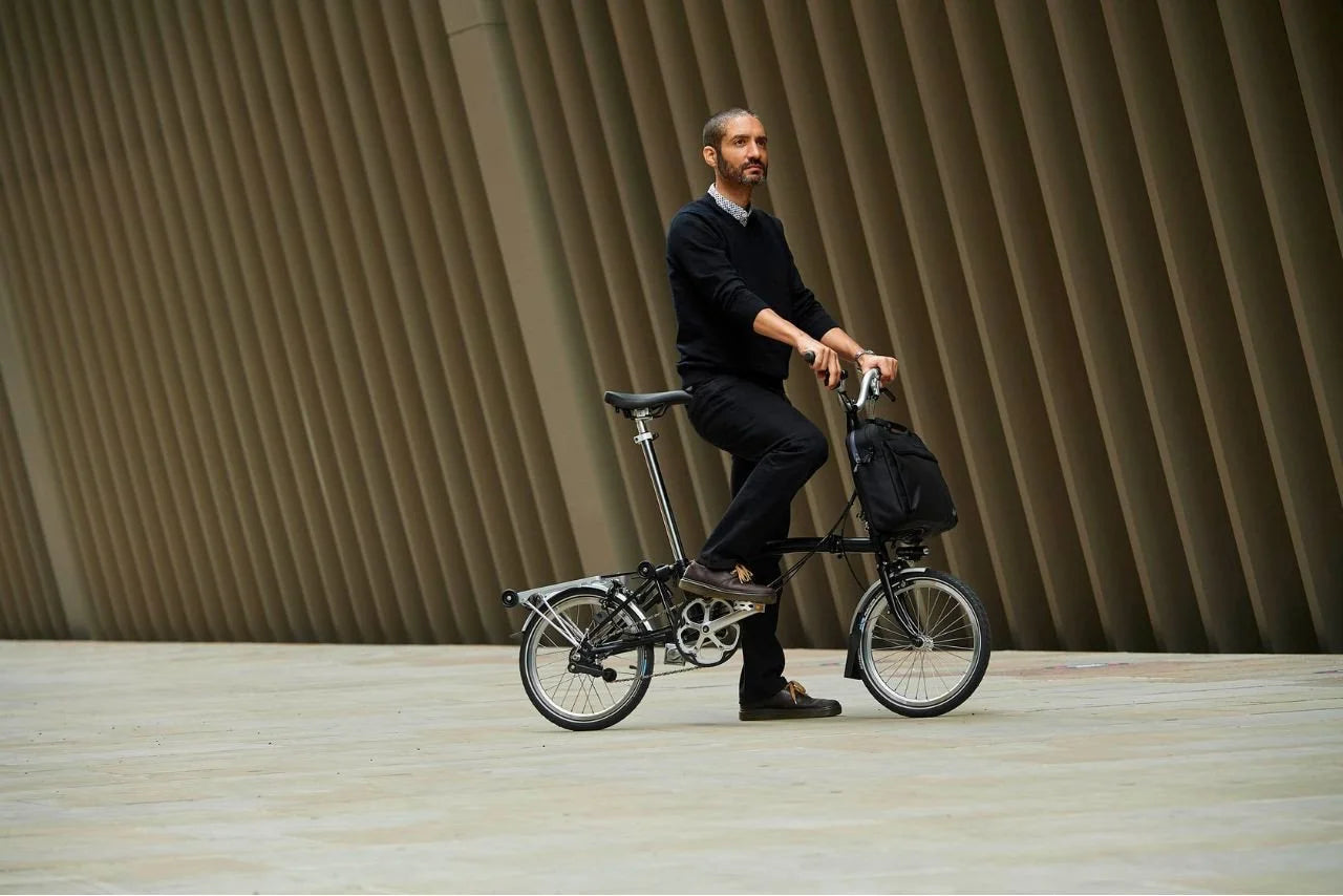 A person on the black Brompton folding bike in the city setting.