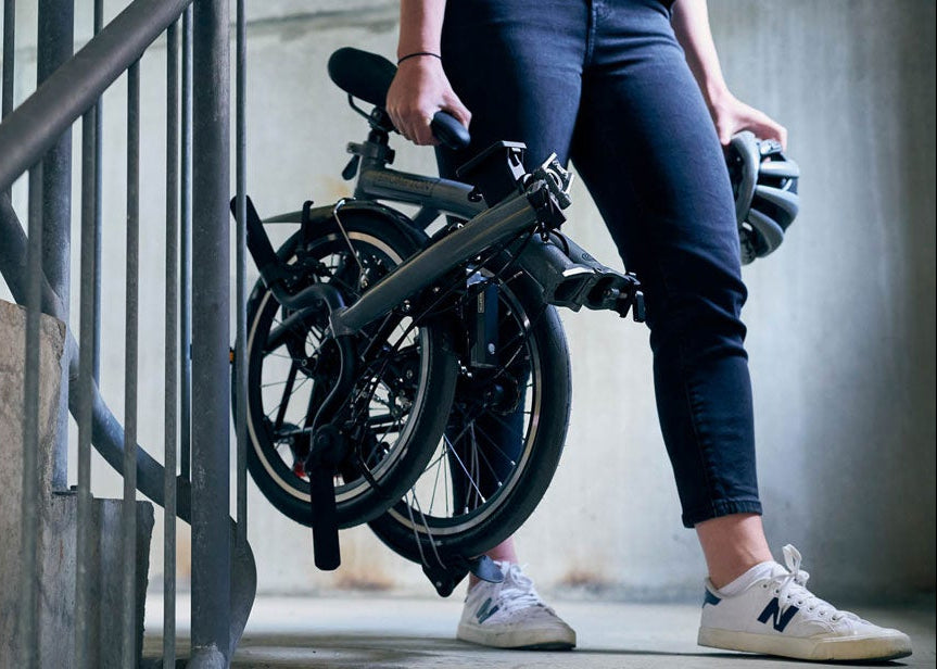 Person holding a folded electric bike against a concrete wall.