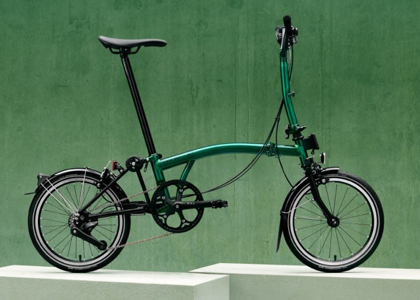 Green Brompton folding bicycle on a white platform with a green background