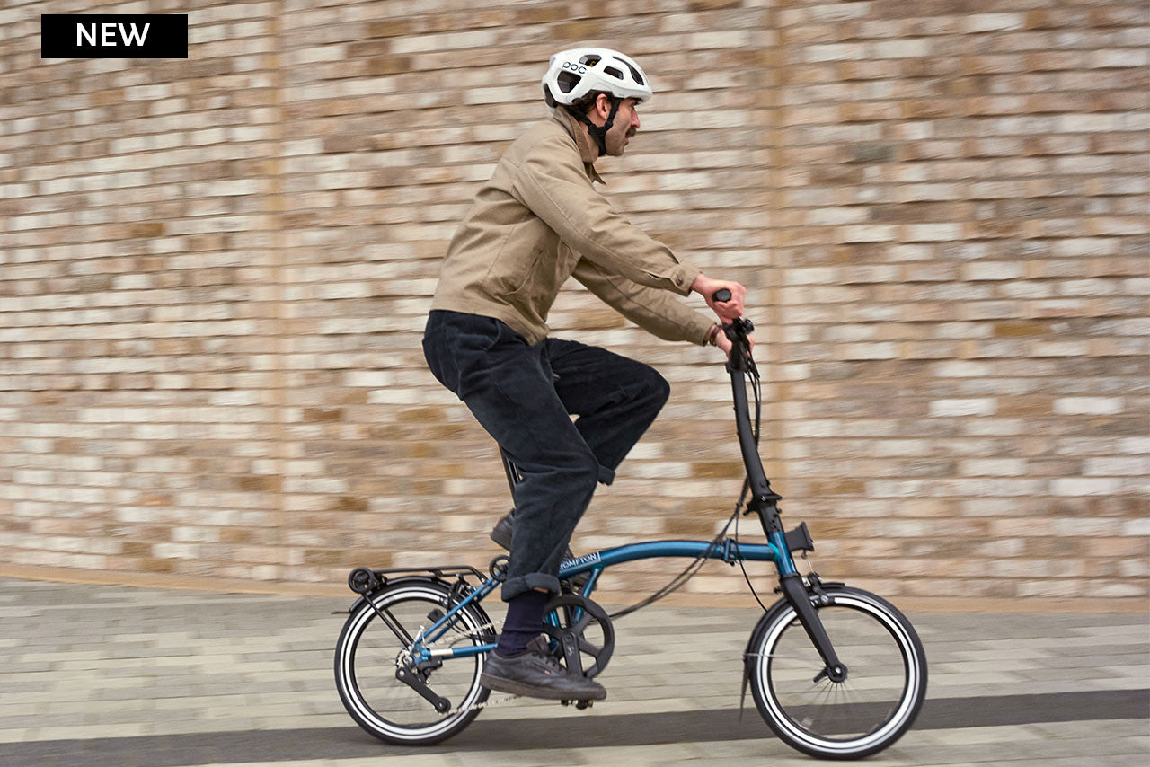 Man riding a blue folding bike against a brick wall.