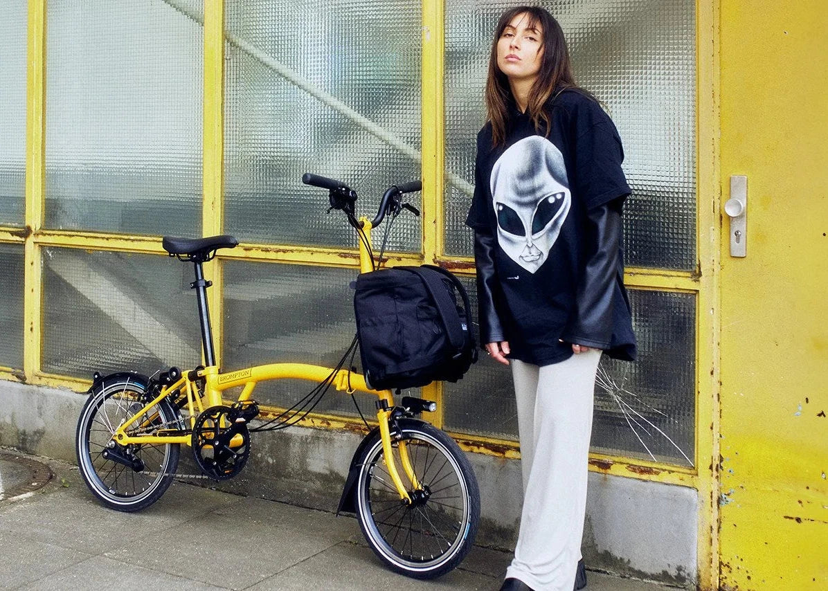 A person standing with Yellow Brompton folding bike in front of the building.