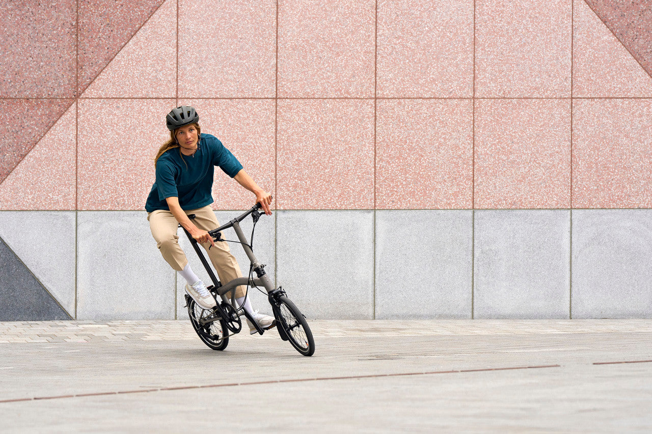 Person riding a folding bicycle on a sidewalk with a geometric-patterned wall in the background