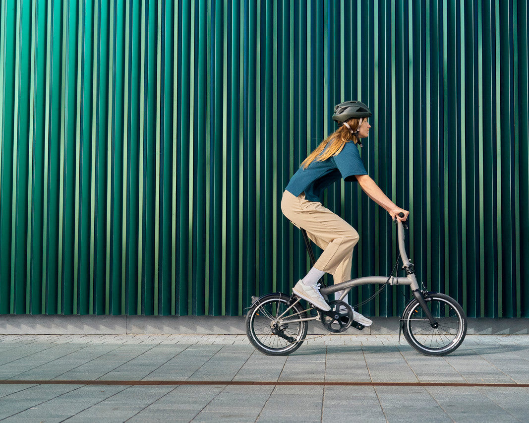 Person riding a Brompton T Line folding bicycle against a green metallic wall