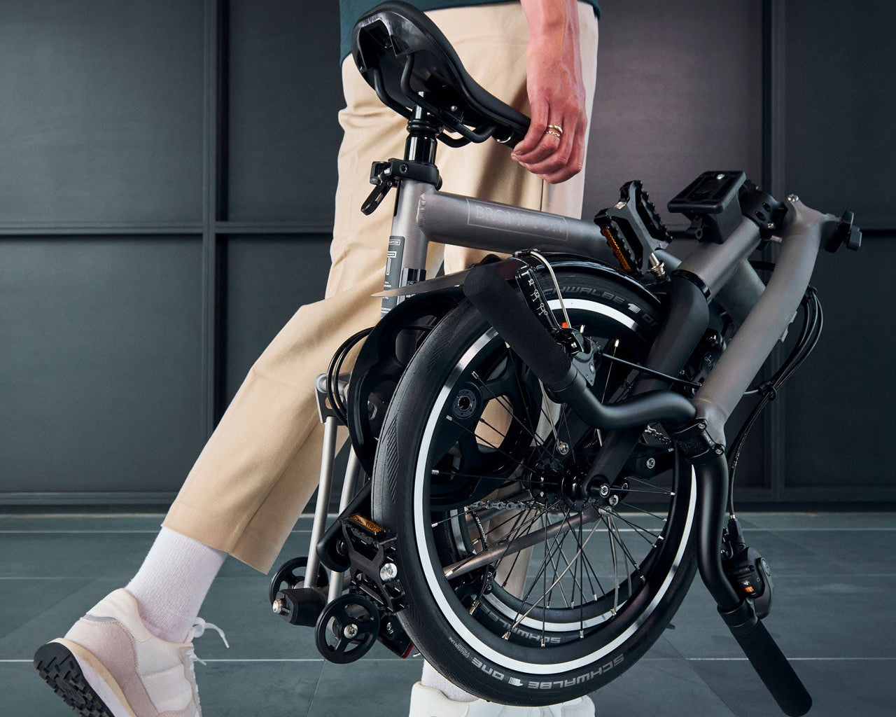 Person holding a folded Brompton T Line bike against a dark background