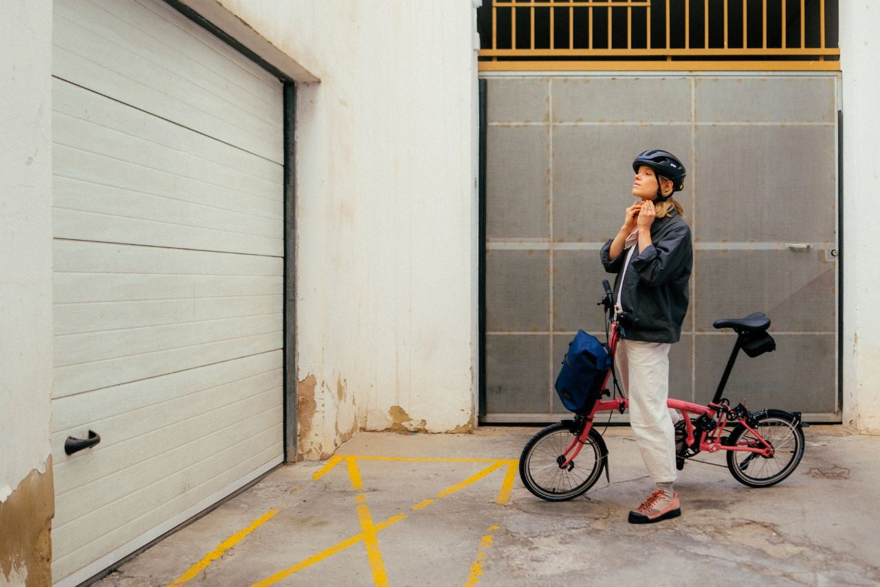 A person standing with a flamingo pink Brompton folding bike by the industrial building.