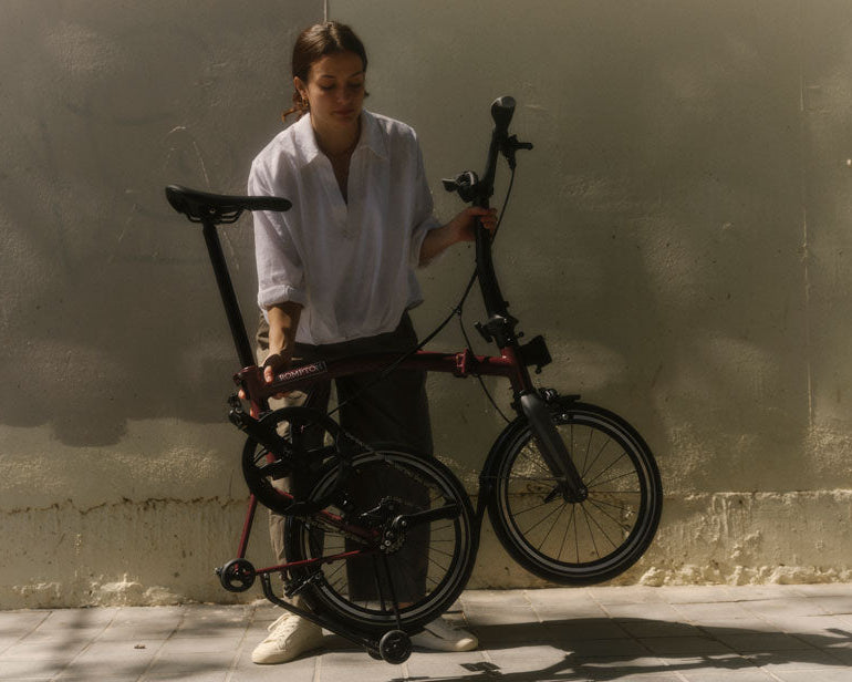 Person holding a folded bicycle against a plain wall