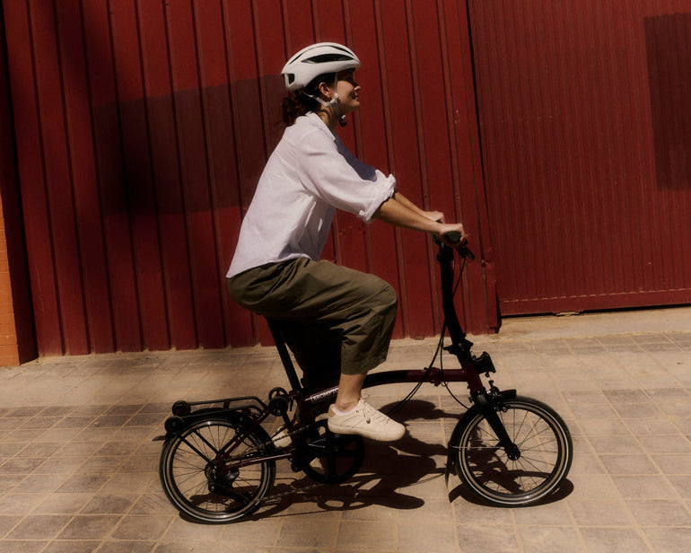 Person riding a Brompton folding bicycle against a red wall.