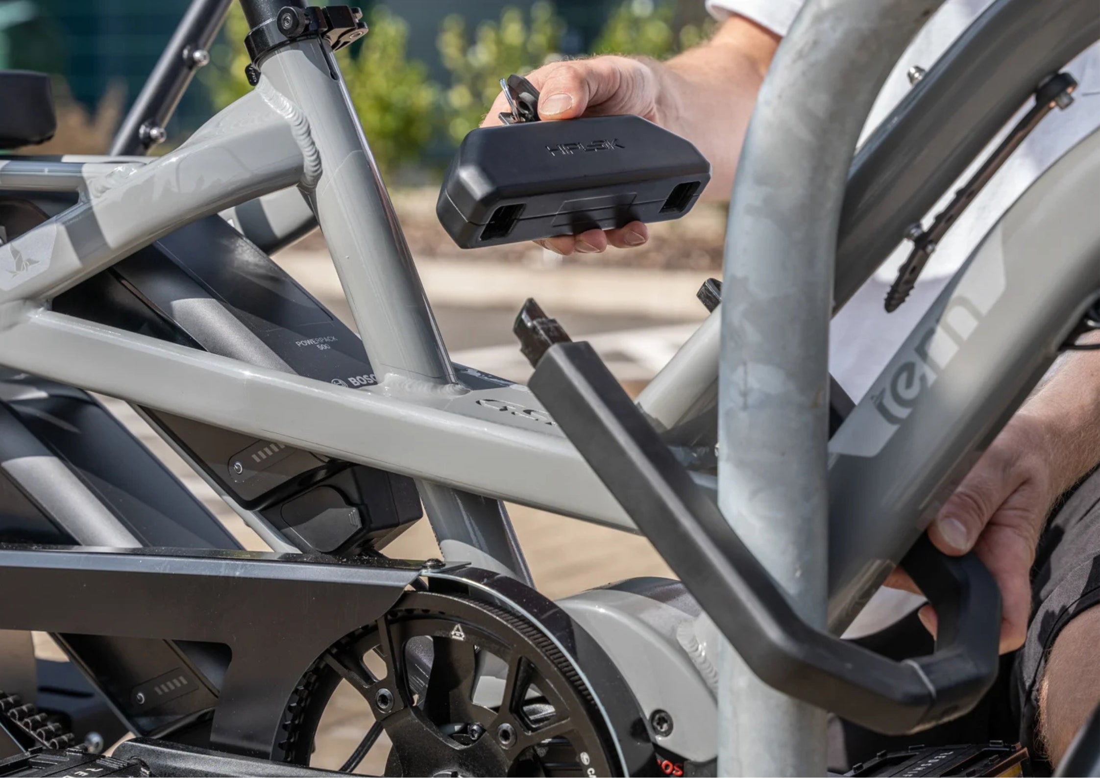 Person attaching a black U-lock  to a gray bicycle frame outdoors.