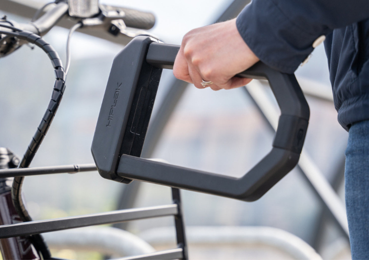 Person holding a black 'Hiplok' branded U-lock on a bicycle with a blurred background