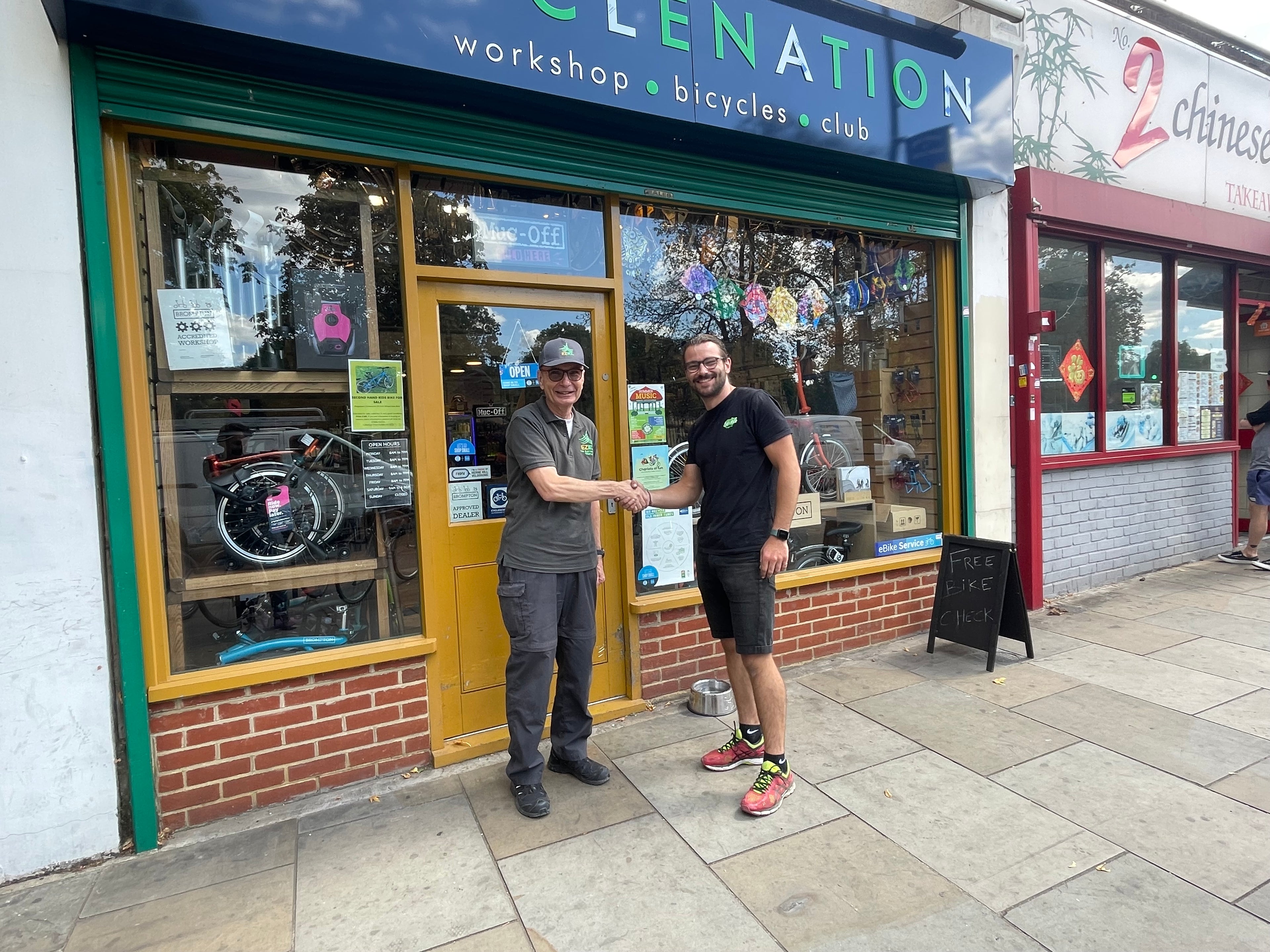 Two men shaking hands outside a bicycle shop named 'Bicyclenation'.