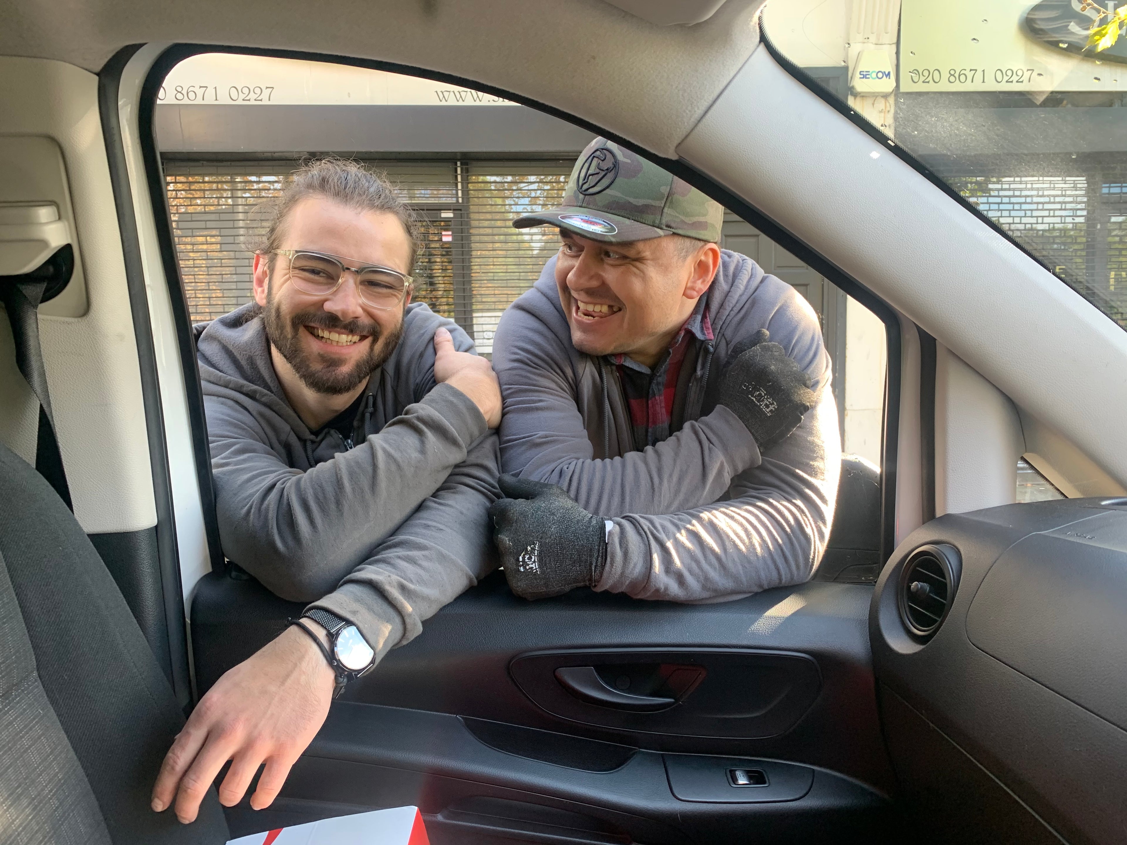 Two men sitting inside a car, smiling at the camera.