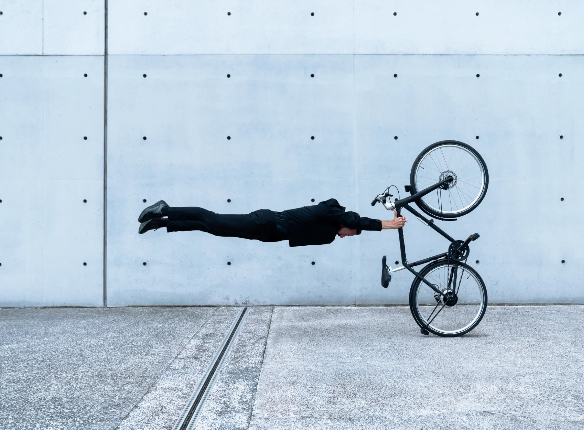 Person lying on the ground with a bicycle against a concrete wall.