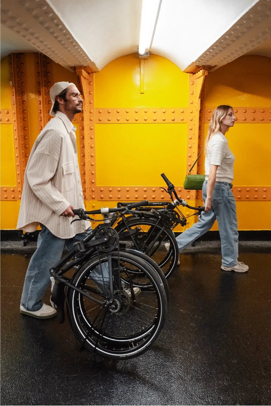 Two people with bicycles in a tunnel with yellow walls.
