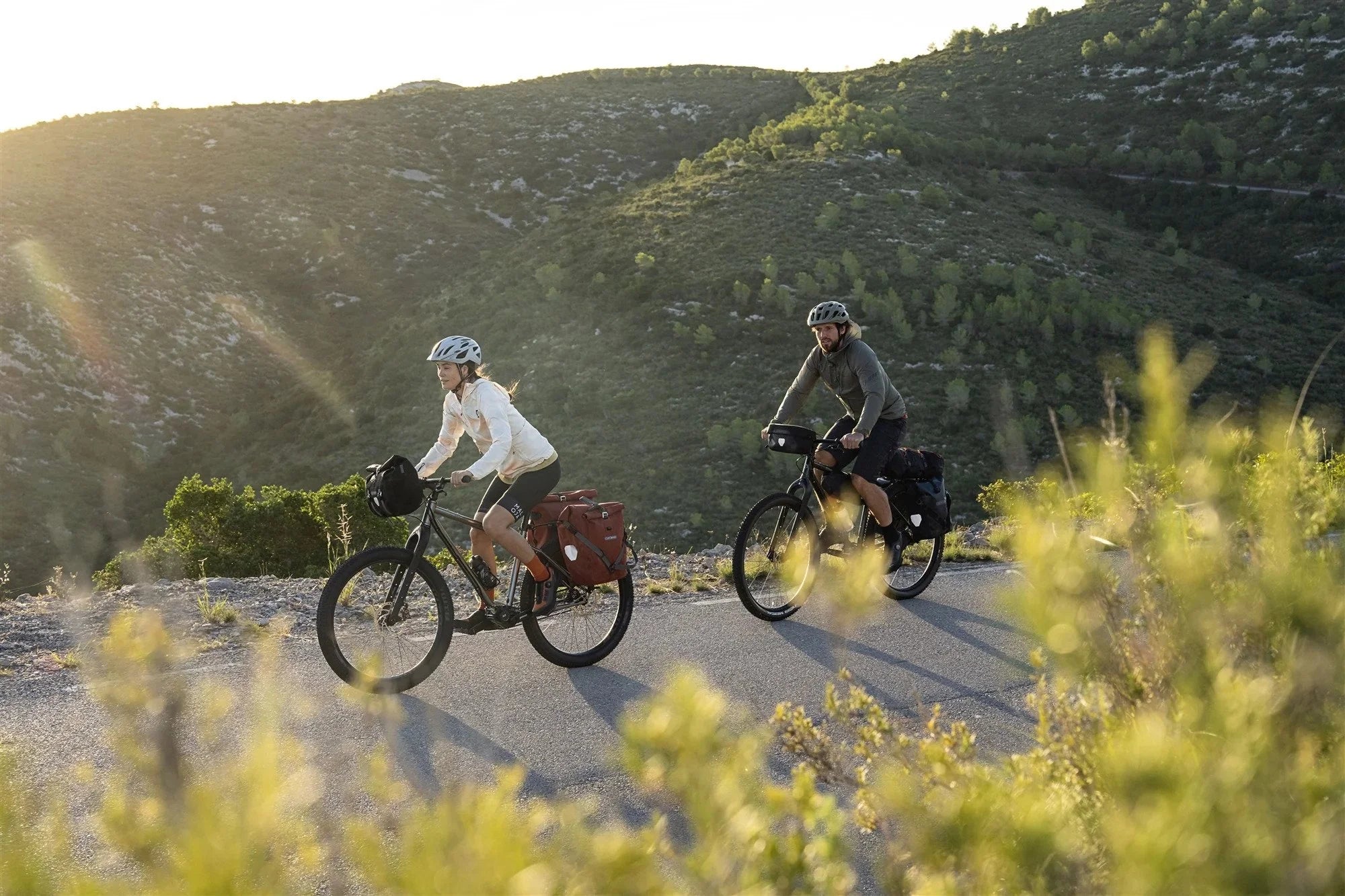 Two cyclists riding on a scenic road with mountains in the background