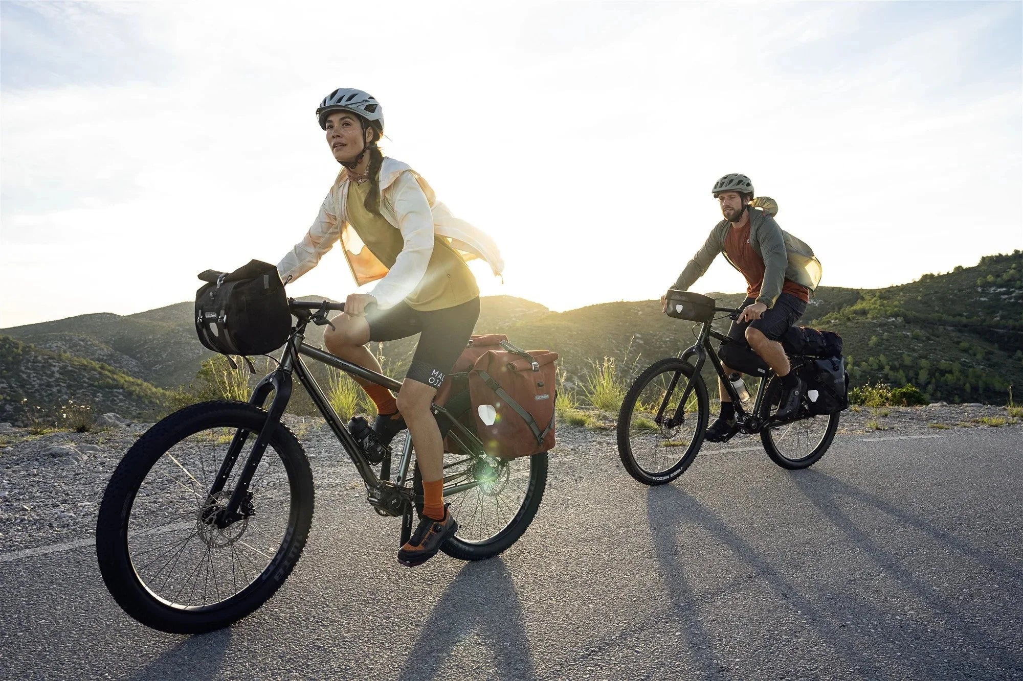 Two people riding bicycles on a road with mountains in the background