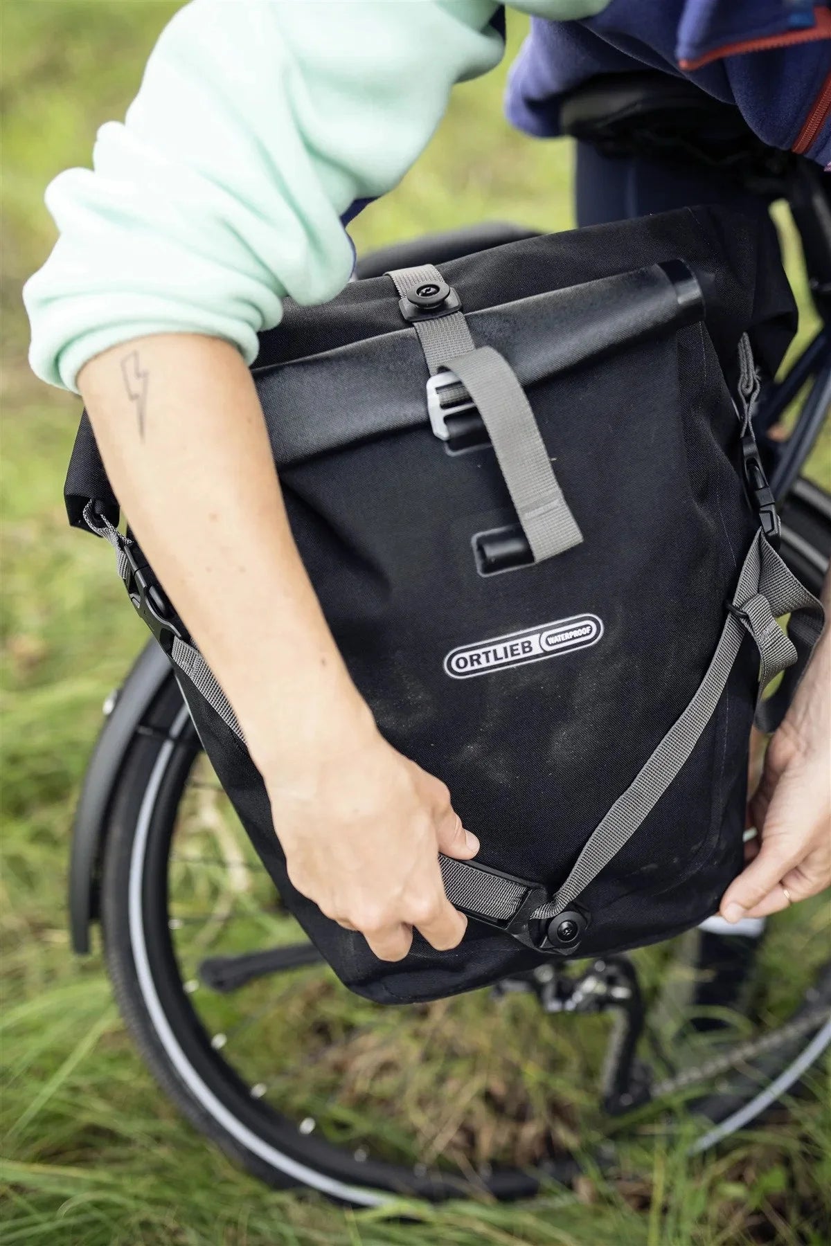 Person holding a black bicycle pannier with 'Ortlieb' branding in an outdoor setting.