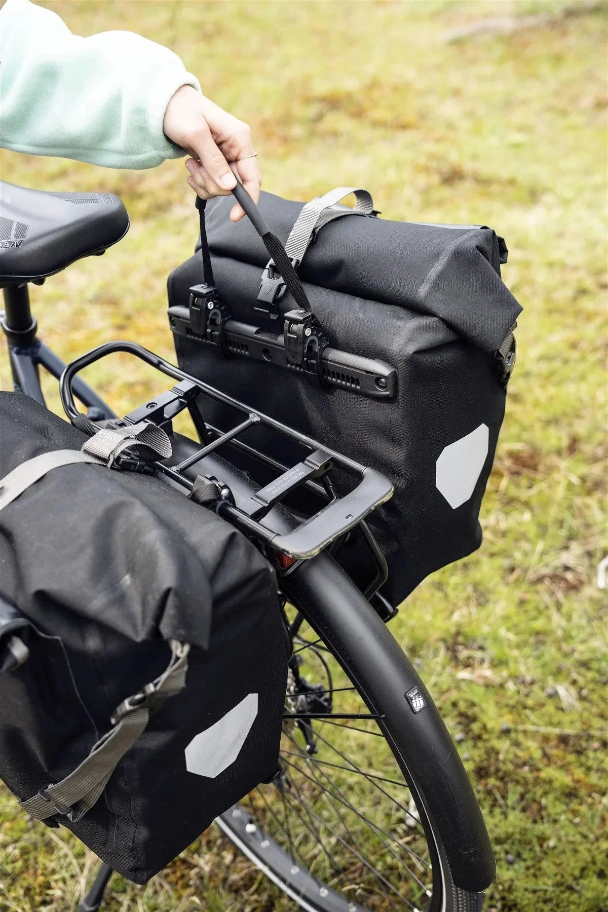 Bicycle with black panniers attached to the back on a grassy background