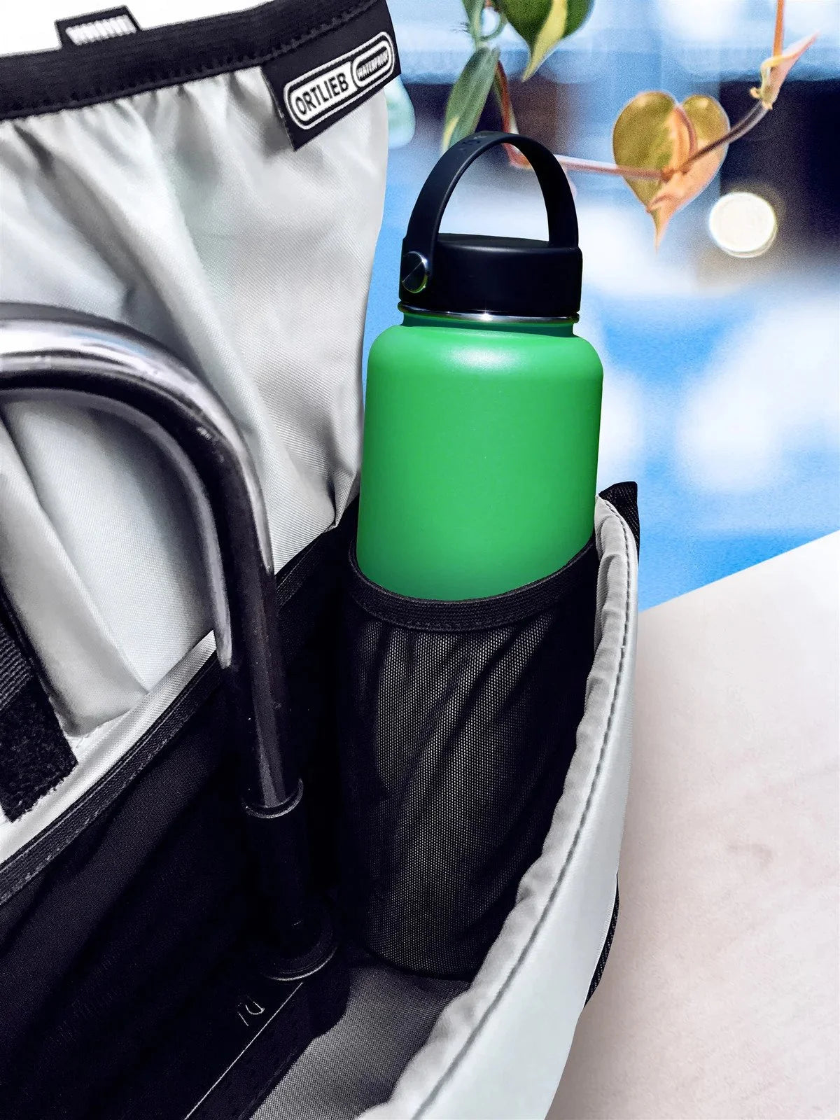 Green water bottle with black cap in a black holder attached to a bag with a blurred background