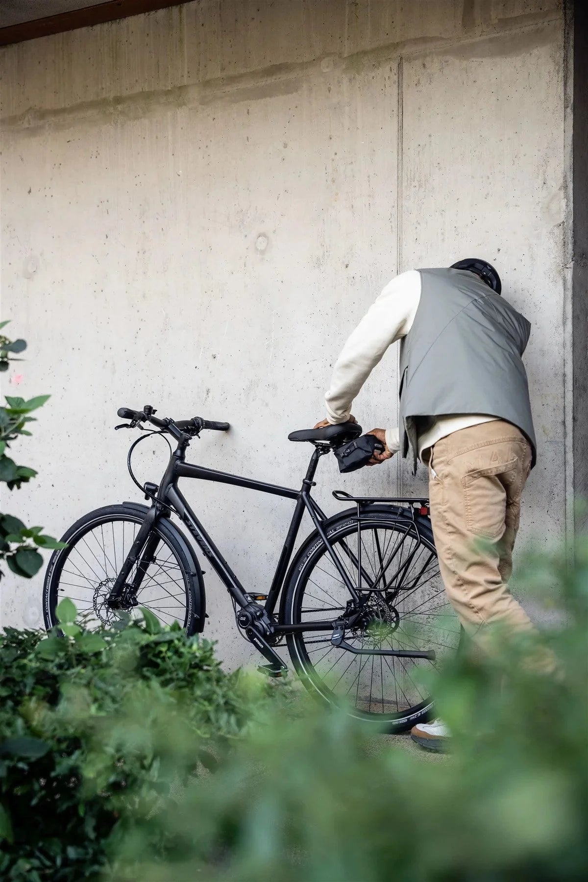 Person leaning against a wall with a black bicycle attaching a saddle bag