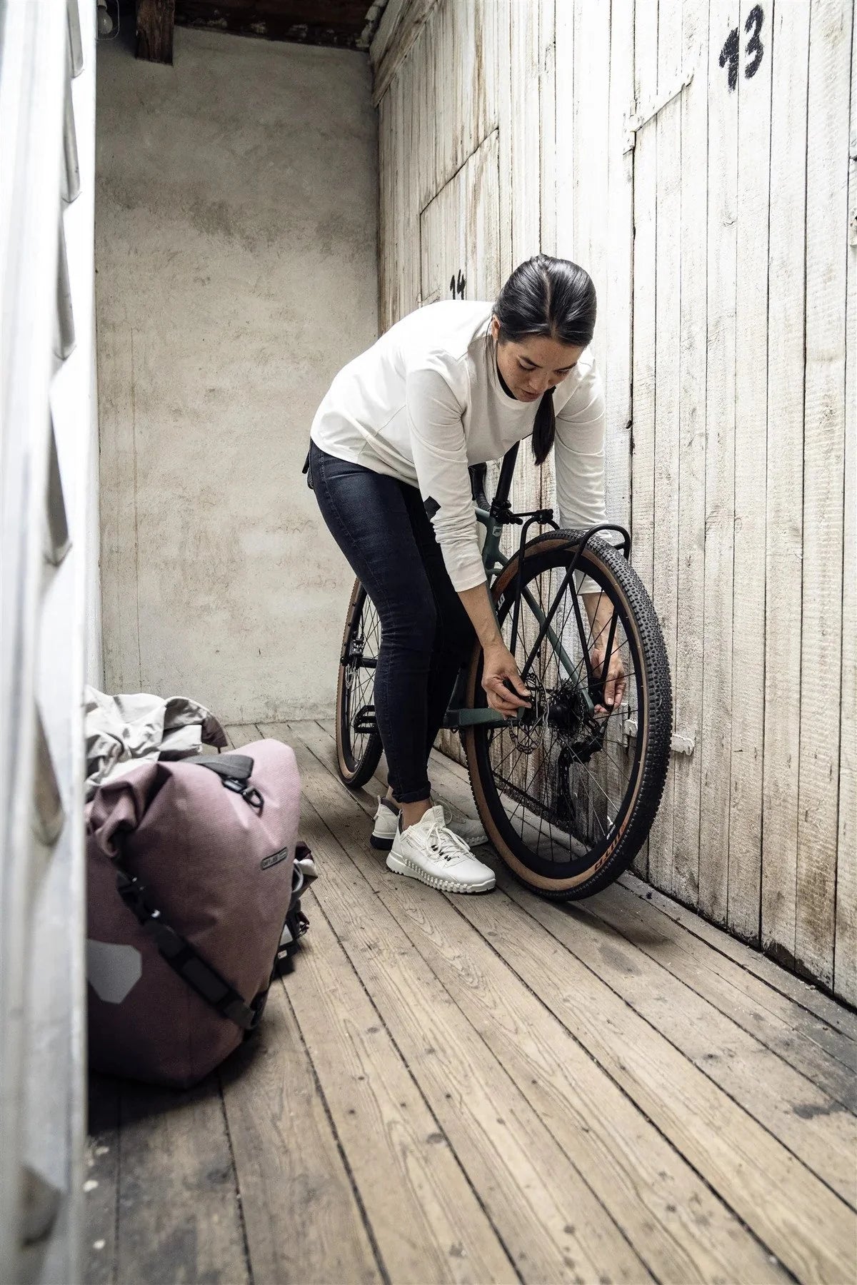 Person adjusting a bicycle in a storage area with wooden floors and white walls.