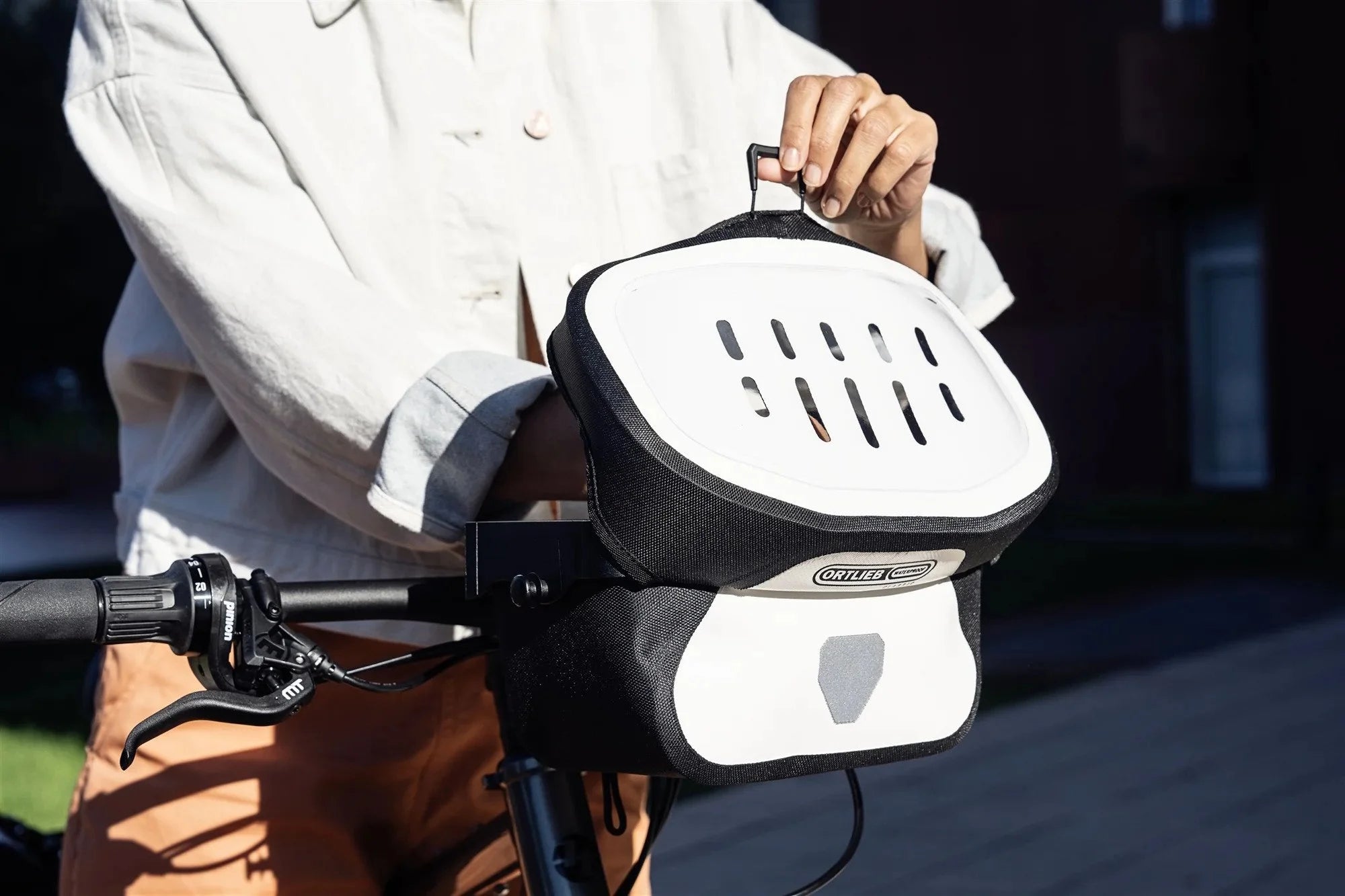 Person holding a black and white Ortlieb handlebar bag with a brand logo on a blurred background