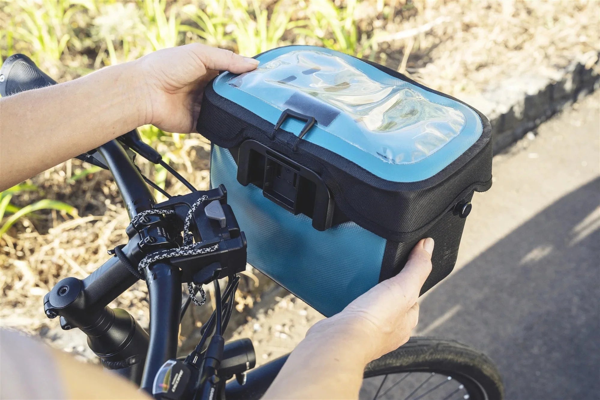 Person attaching a gray and black bike storage box to a bicycle.