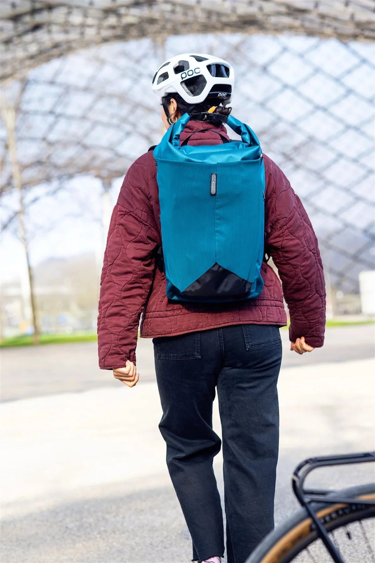 Person wearing a blue backpack and helmet, walking outdoors with a blurred background
