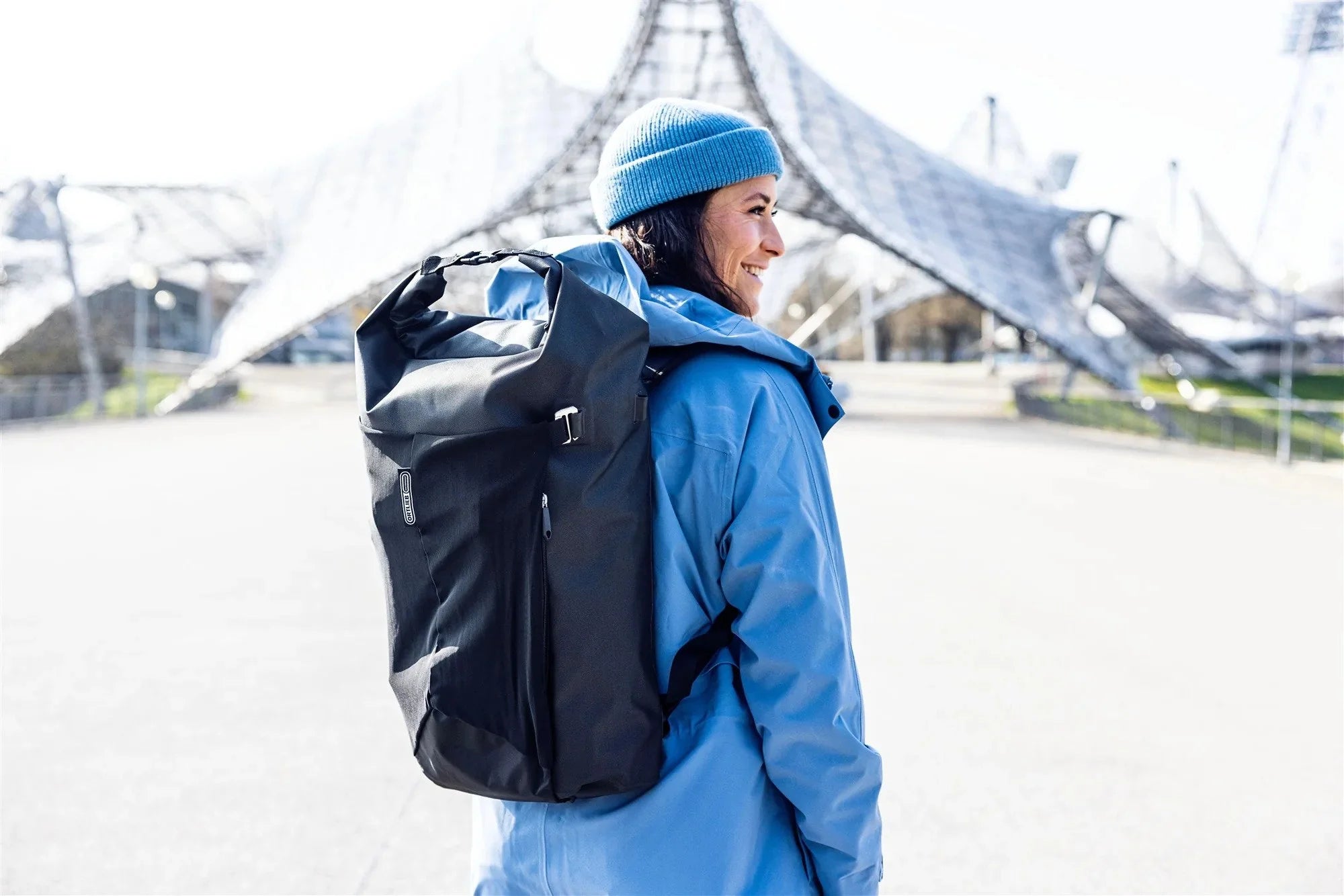 Person wearing a blue jacket and blue beanie with a black backpack, standing outdoors.