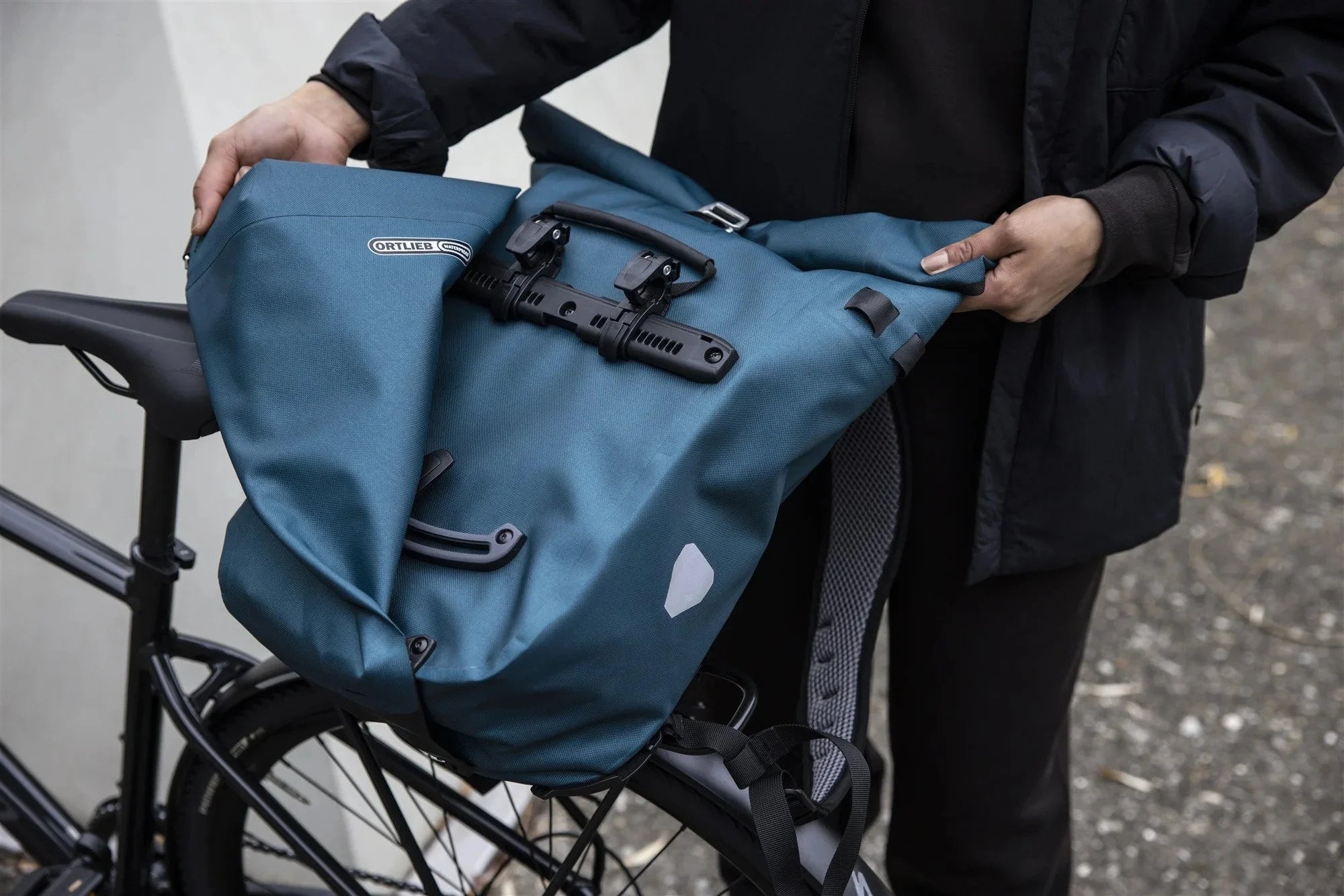 Person holding a blue pannier bag attached to a bicycle