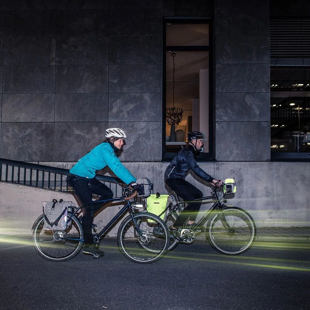 Two cyclists riding bicycles at night in an urban setting.