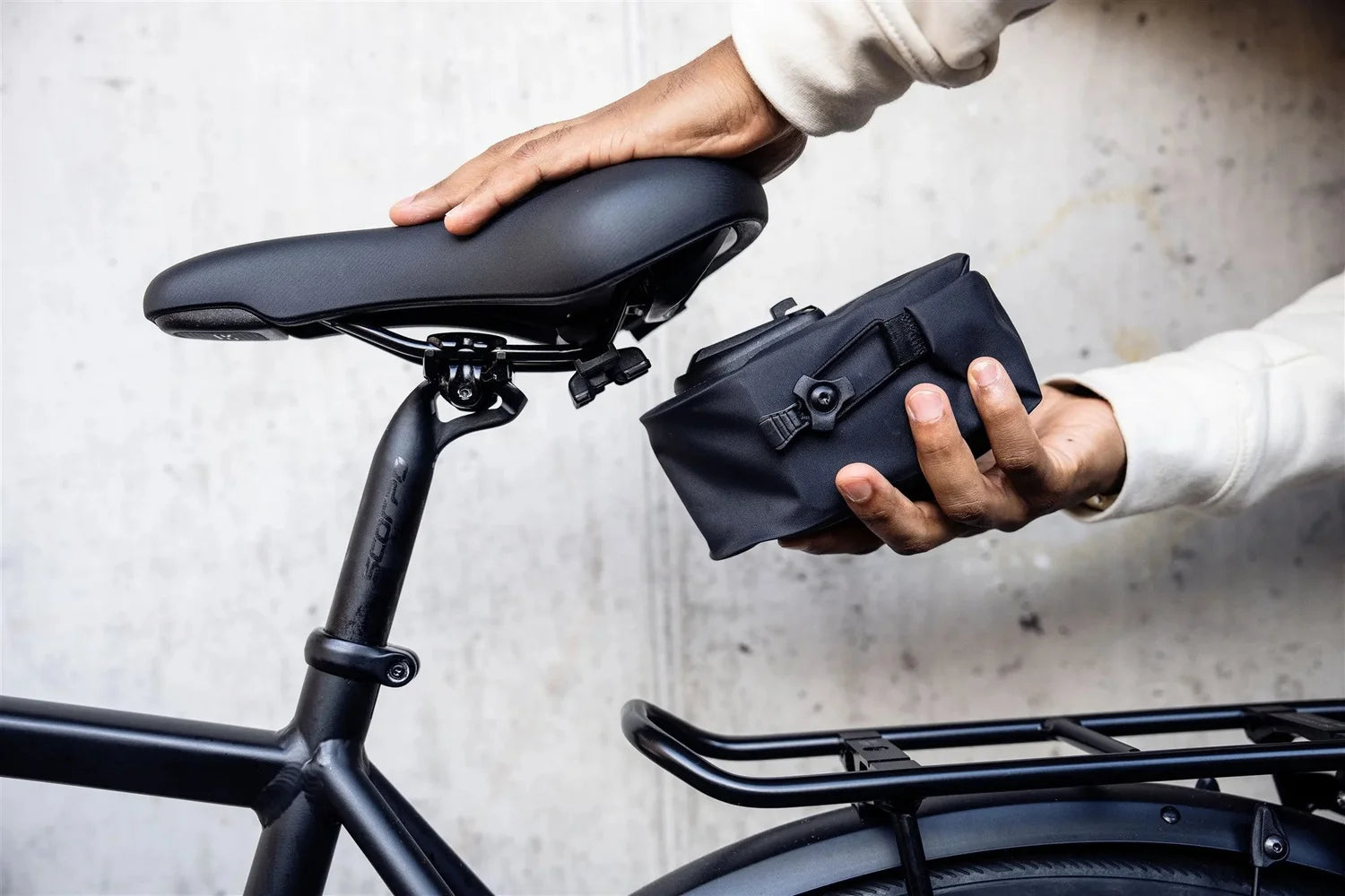 Person attaching a black bike bag to a bicycle with a plain background