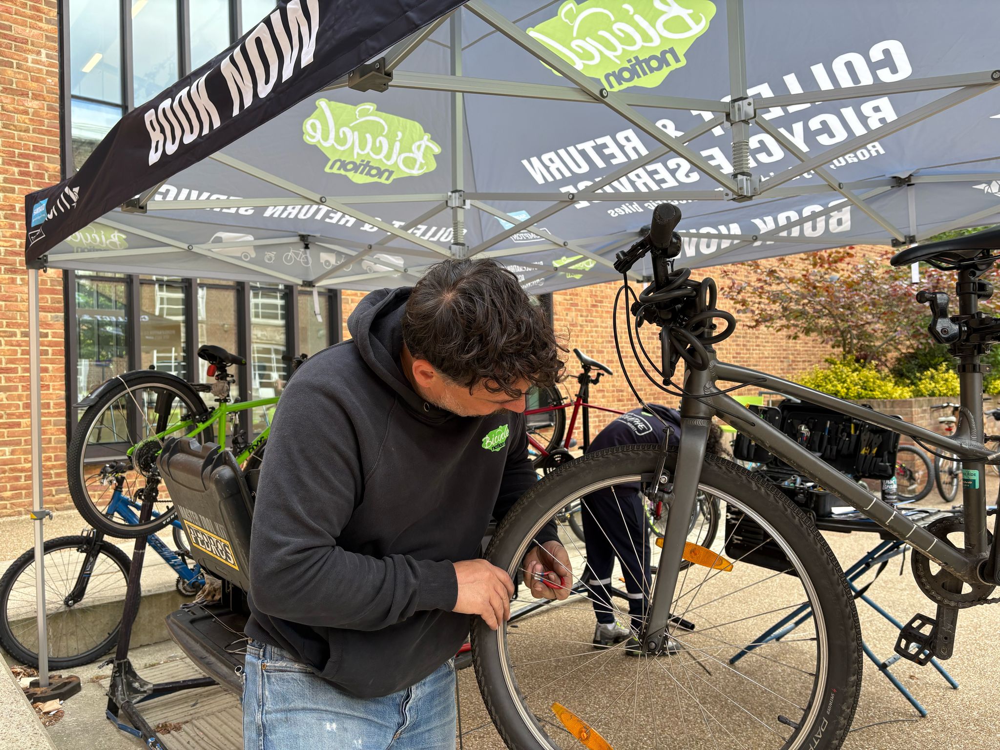 Person working on a bicycle under a tent with cycling-related branding.