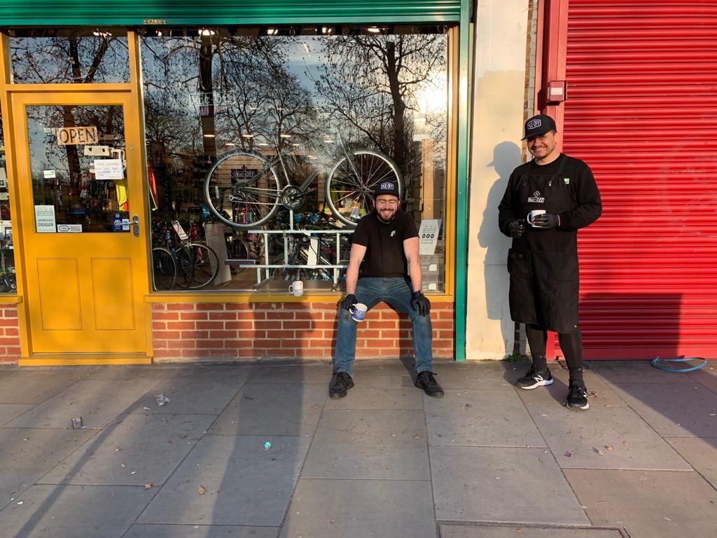 Two men standing outside a bike shop with bicycles displayed in the window.